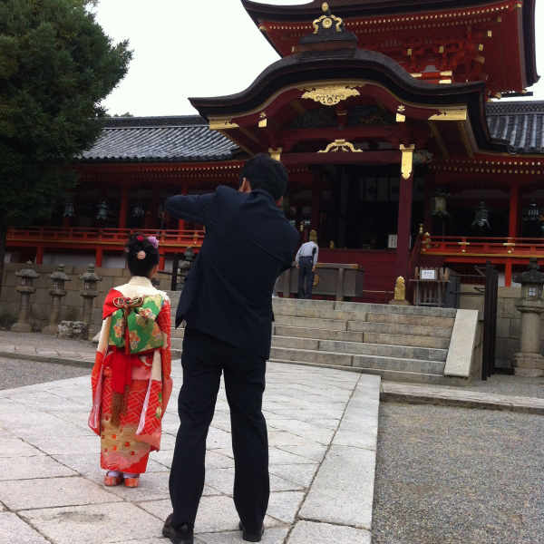 神社の本殿の前で娘の写真を撮る父親